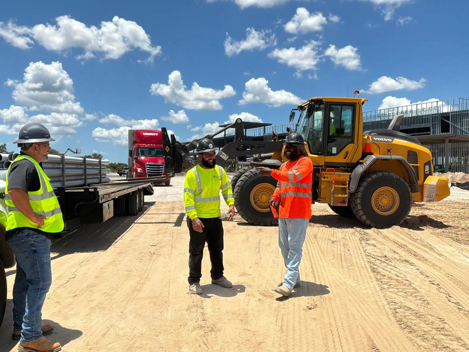 Field team coordinating beside a flatbed delivery and wheel loader