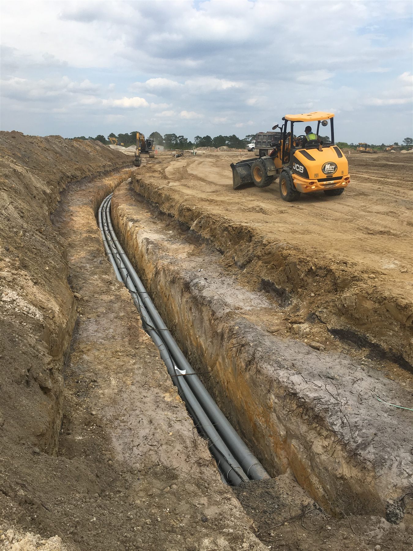 Heavy equipment grading an active construction site beside underground utility work