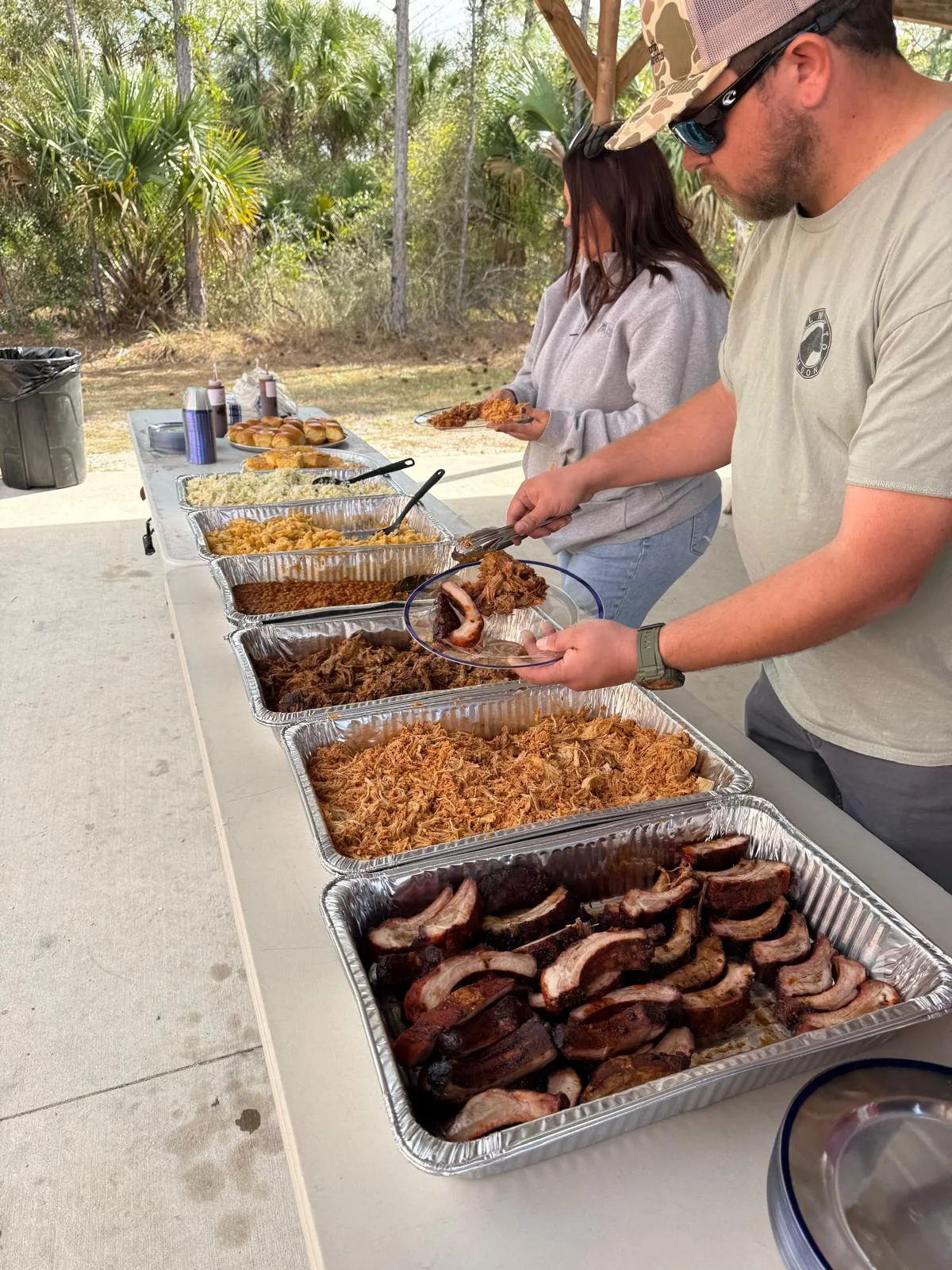 People serving food from an outdoor buffet at the 3rd Annual Bravo Shotgun Blast
